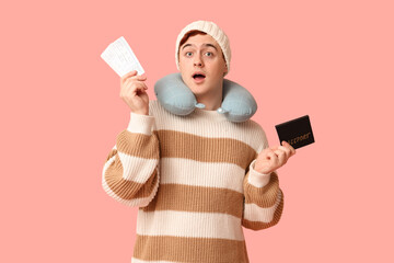 Wall Mural - Handsome young shocked man with travel pillow, passport and ticket on pink background. Winter vacation concept