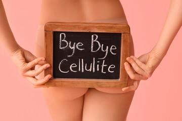 Wall Mural - Beautiful young woman holding board with text BYE BYE CELLULITE on pink background, back view