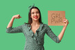 Beautiful young happy pin-up woman holding paper sheet with text GIRL POWER and showing muscles on green background