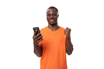 Wall Mural - young african man dressed in orange t-shirt holding phone and chatting on social media