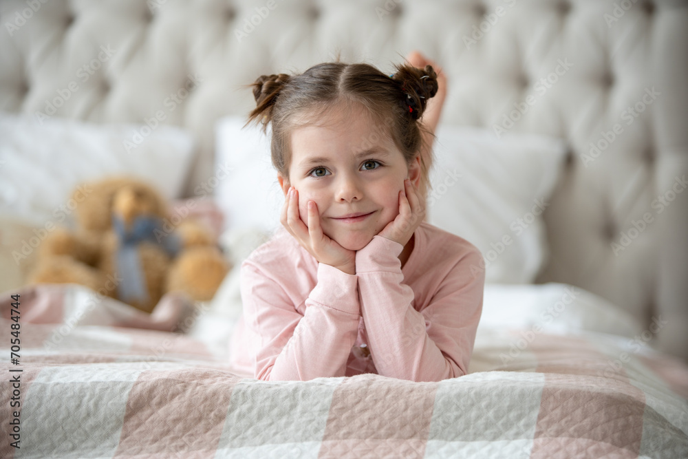 Cute little girl in pajama hugging her toy hare on the bed at home ...