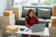 © amnaj - Smiling young business owner woman prepare parcel box and standing check online orders of product for deliver to customer on laptop computer. Shopping Online concept.
