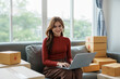 © amnaj - Smiling young business owner woman prepare parcel box and standing check online orders of product for deliver to customer on laptop computer. Shopping Online concept.