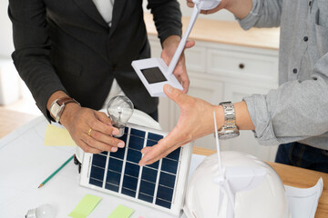 Wall Mural - Businessman holding light bulbs, solar panel and wind turbine with colleague sitting at office.