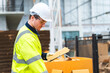 © chokniti - Engineer wearing safety vest controlling industrial machine working, talking with assistant worker checking first for labour with laptop computer, Officer setting a technology system in factory.