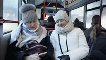 Two Friends Of Different Ages Are Traveling On A Bus, Looking At A Smartphone And Laughing.