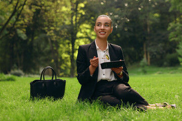 Canvas Print - Lunch time. Happy businesswoman with container of salad on green grass in park