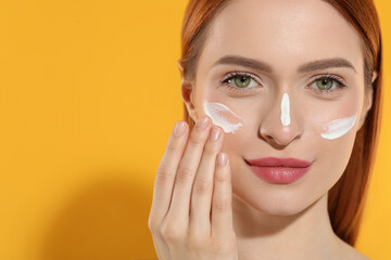 Poster - Beautiful young woman with sun protection cream on her face against orange background, closeup. Space for text