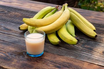 Wall Mural - delicious bananas and juice in glass containing lots of vitamin c are good to eat on a brown wooden background