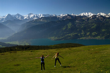 Niederhorn, Emmental Alps, Bernese Oberland, canton Bern, Switzerland, Europe : two young female tourists, panoramic view from the top on Thun Lake and Jungfrau-Aletsch mountains area, UNESCO