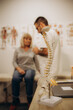 A happy senior woman lies on an examination couch while a chiropractor, osteopath or physiotherapist examines her back. Treatment of osteoporosis, physiotherapy, concept of physical therapy.