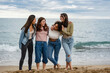 © PintoArt - group of young adult friends standing with the sea in the background talking to each other