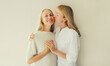 Portrait of adult daughter kissing her happy smiling caucasian middle aged mother on studio background