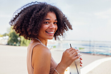 Wall Mural - Happy african american teen girl drinking lemonade in open air cafe.