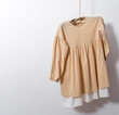 © dvulikaia - Child's dress made of natural materials hangs on wooden branch against white wall background. Copy space. Eco design concept.