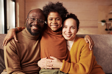 Wall Mural - Young smiling intercultural couple in casualwear and their happy son looking at camera while enjoying leisure or weekend in cottage