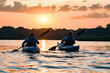 © apratim - Two kayakers paddle on a tranquil lake against the stunning backdrop of a golden sunset.