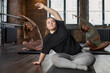 © pressmaster - Young active woman with mental disability doing side bends while sitting on mat in front of camera against two intercultural women