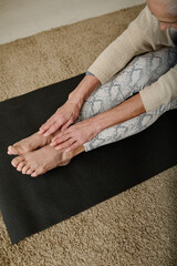 Wall Mural - Above angle of senior active barefoot woman sitting on black mat and stretching arms forwards while doing physical exercise