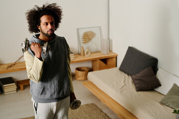 Wall Mural - Active guy lifting heavy metallic dumbbell while standing on the floor of bedroom in front of camera and doing morning exercises