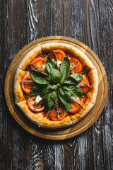 Wall Mural - Appetizing pizza with tomatoes, anchovies and basil on a wooden background. Fluffy pizza with crispy sides.