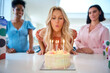 © Monkey Business - Mature Woman At Home Celebrating Birthday With Friends And Blowing Out Candles On Cake
