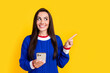 Photo of optimistic promoter young charming blogger businesswoman point finger empty space with phone isolated on yellow color background