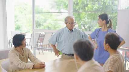 Wall Mural - Asian nurse stand and guide to senior or elderly man to exercise his waist in front of group of senior people in clinic or hospital room with day light.