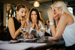 © Marko Geber - Women friends excitedly looking at smartphone in restaurant