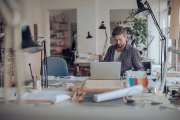 Young male architect working on laptop in office