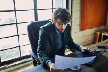 Wall Mural - Concentrated businessman reviewing documents and working on laptop in office