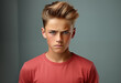 Angry teenage boy in a red T-shirt with a serious expression on his face isolated on gray background with copy space