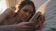 © stockbusters - Closeup sleepy girl message smartphone in bed. Calm awake female checking mobile