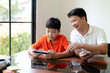 © mojo_cp - Father and son playing video games on smartphone together with enjoying family activity at home