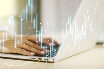 Multi exposure of abstract creative financial graph with hand typing on laptop on background, forex and investment concept