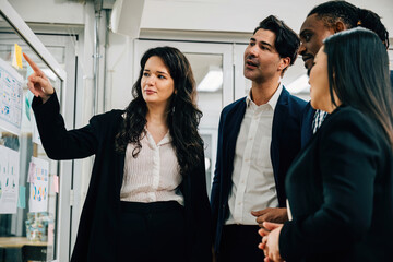 Wall Mural - Young creative businesswoman stands with her colleagues, brainstorming and planning new ideas on sticky notes over glass wall. teamwork, collaboration creative thinking are key to achieving success.