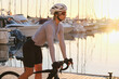 Fit woman cyclist is donned in a complete cycling kit,riding an e-bicycle against the backdrop of a yacht club during the sunset.Training an E-Bike.Sport motivation.Active lifestyle concept.Calp,Spain