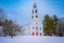 A Tall White Church With A Clock Tower, Rainbow Flag, And Red Doors On The Snow-covered Hilltop