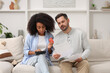 © New Africa - Confused couple with debt notifications, calculator and credit card planning budget at home. Financial problem
