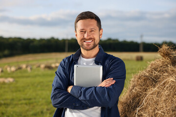 Poster - Smiling farmer with tablet near hay bale on farm