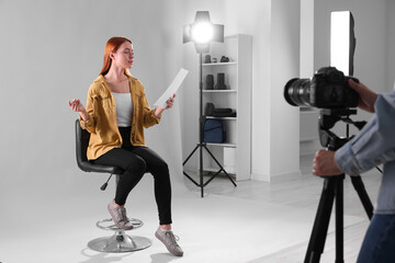 Poster - Casting call. Woman with script performing while camera operator filming her against light grey background in studio