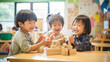 日本の幼稚園児3人が私服で木の積み木を使って笑顔で遊んでいる写真、背景保育ルーム、木育/幼児教育