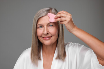 Wall Mural - Woman massaging her face with rose quartz gua sha tool on grey background