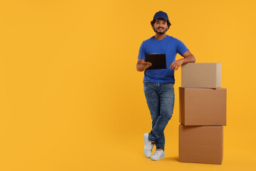 Poster - Happy courier with clipboard and stack of parcels on orange background, space for text