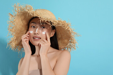 Canvas Print - Beautiful young woman in straw hat with sun protection cream on her face against light blue background, space for text