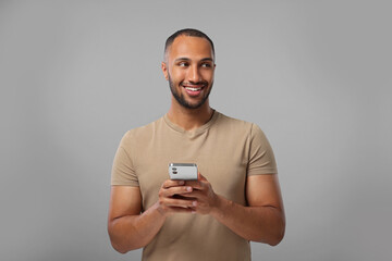 Wall Mural - Happy man sending message via smartphone on grey background