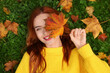 © New Africa - Smiling woman lying on grass and covering eye with autumn leaf, top view