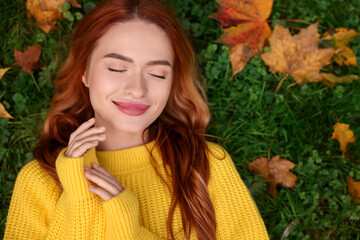 Wall Mural - Beautiful woman lying on grass among autumn leaves, top view