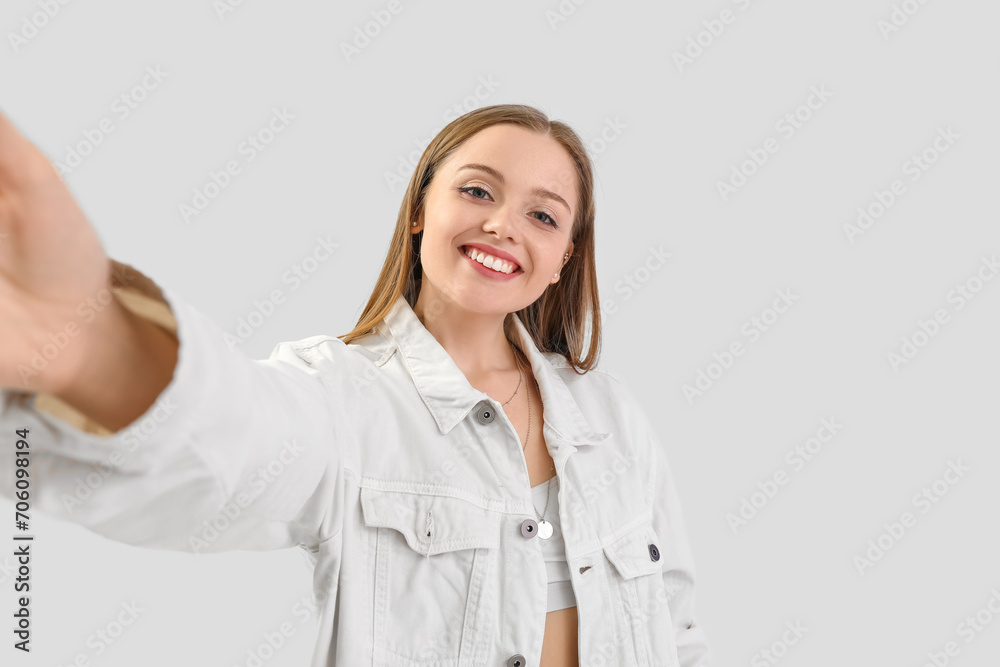 Pretty young woman in stylish clothes taking selfie on light background