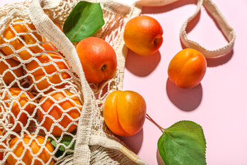 String bag with fresh apricots and leaves on pink background